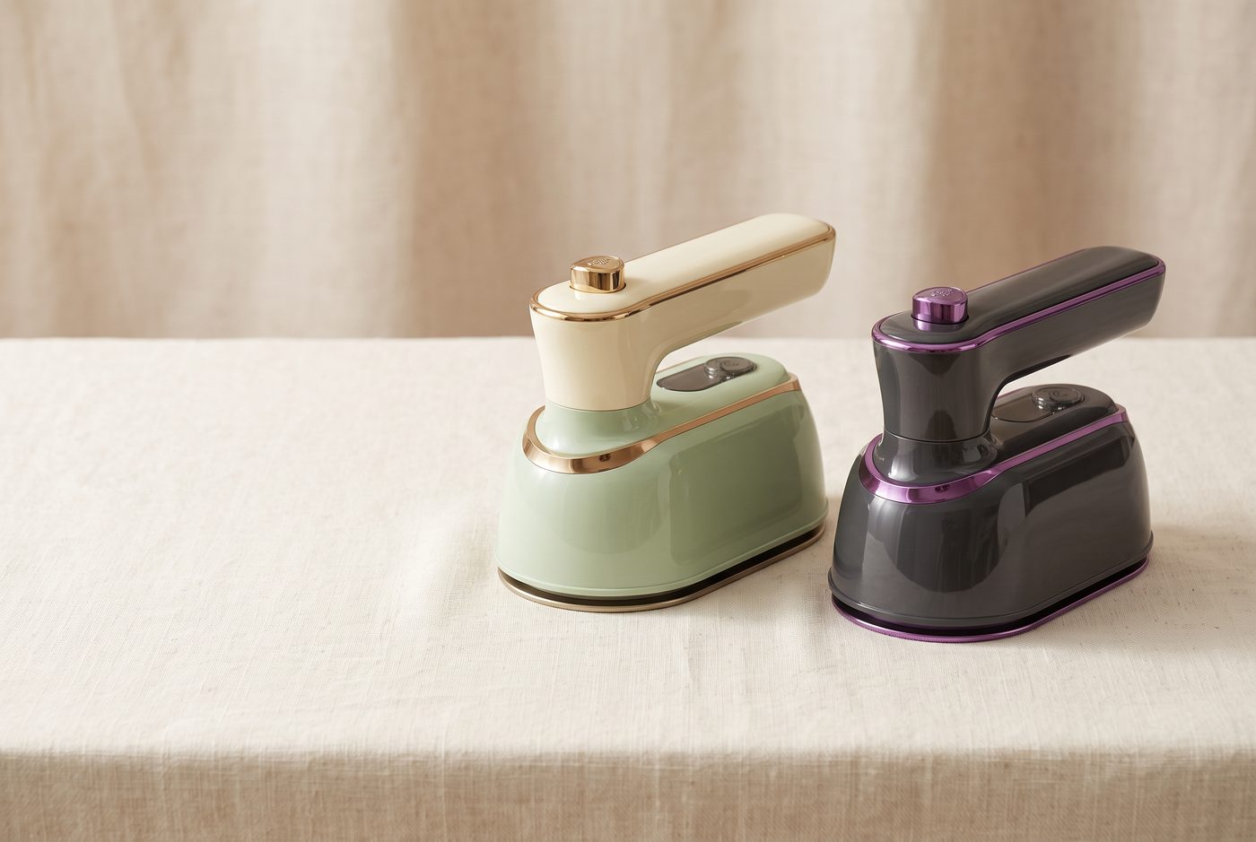 The Lisvelle Mini Steam Iron in Sage and Charcoal side by side on a linen table