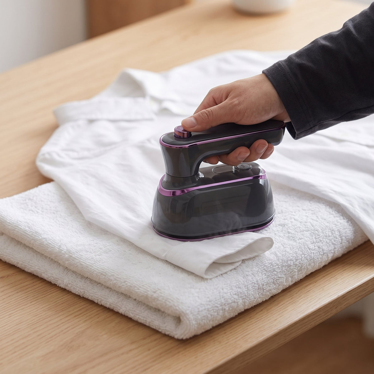 A hand pressing a white shirt cuff on a folded towel with the Charcoal mini steam iron
