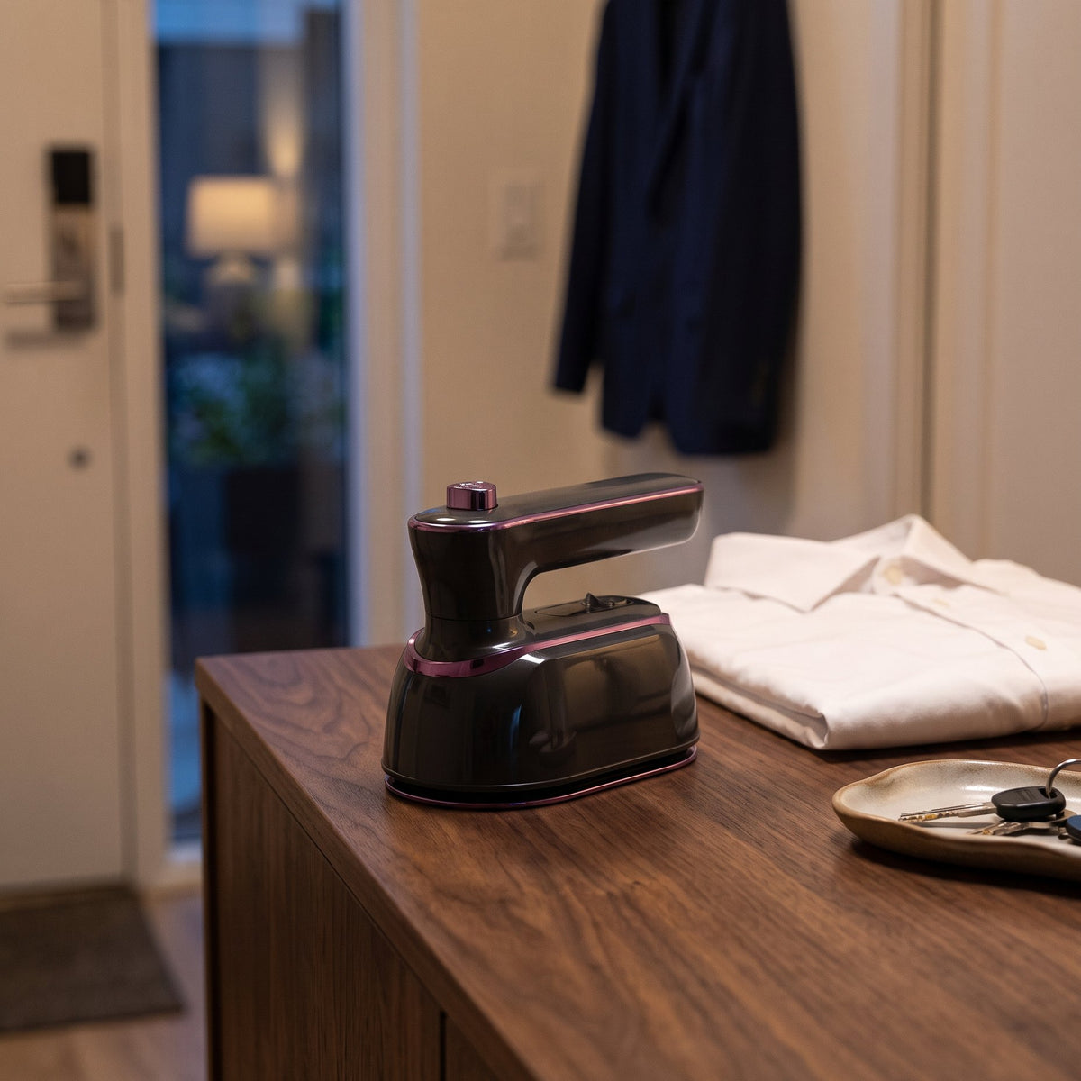 The Charcoal mini steam iron on a walnut console in an apartment entryway
