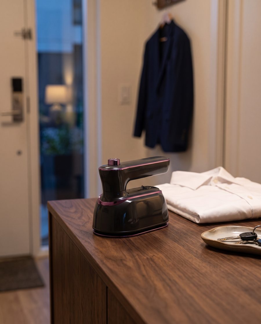 The Charcoal mini steam iron on a walnut console beside a folded white shirt